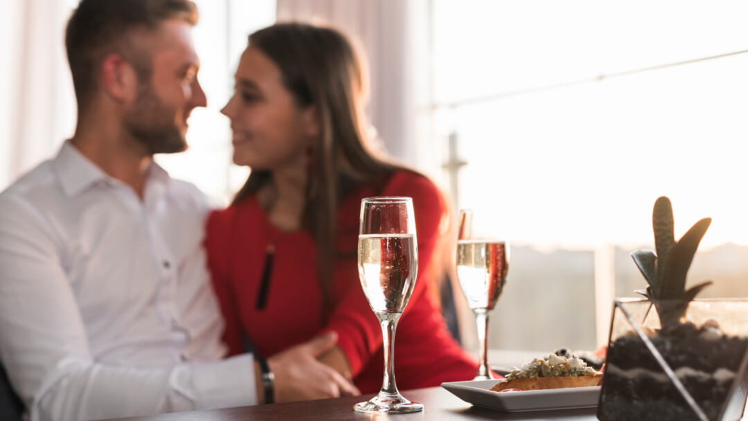 Un homme et une femme assis à une table, levant des flûtes de champagne pour un toast.